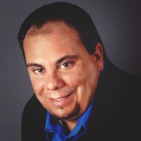 Craig Weiss portrait. Man with short brown hair, wearing a blue collared shirt and black jacket.