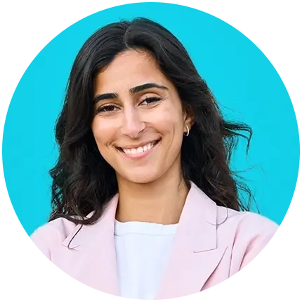 Portrait of a smiling woman with long, wavy black hair wearing a light pink blazer over a white shirt.