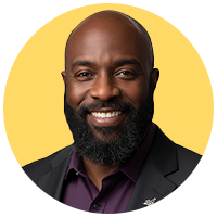 Portrait of a bald man with a bushy, black beard, wearing a charcoal-grey suit jacket and dark purple shirt.