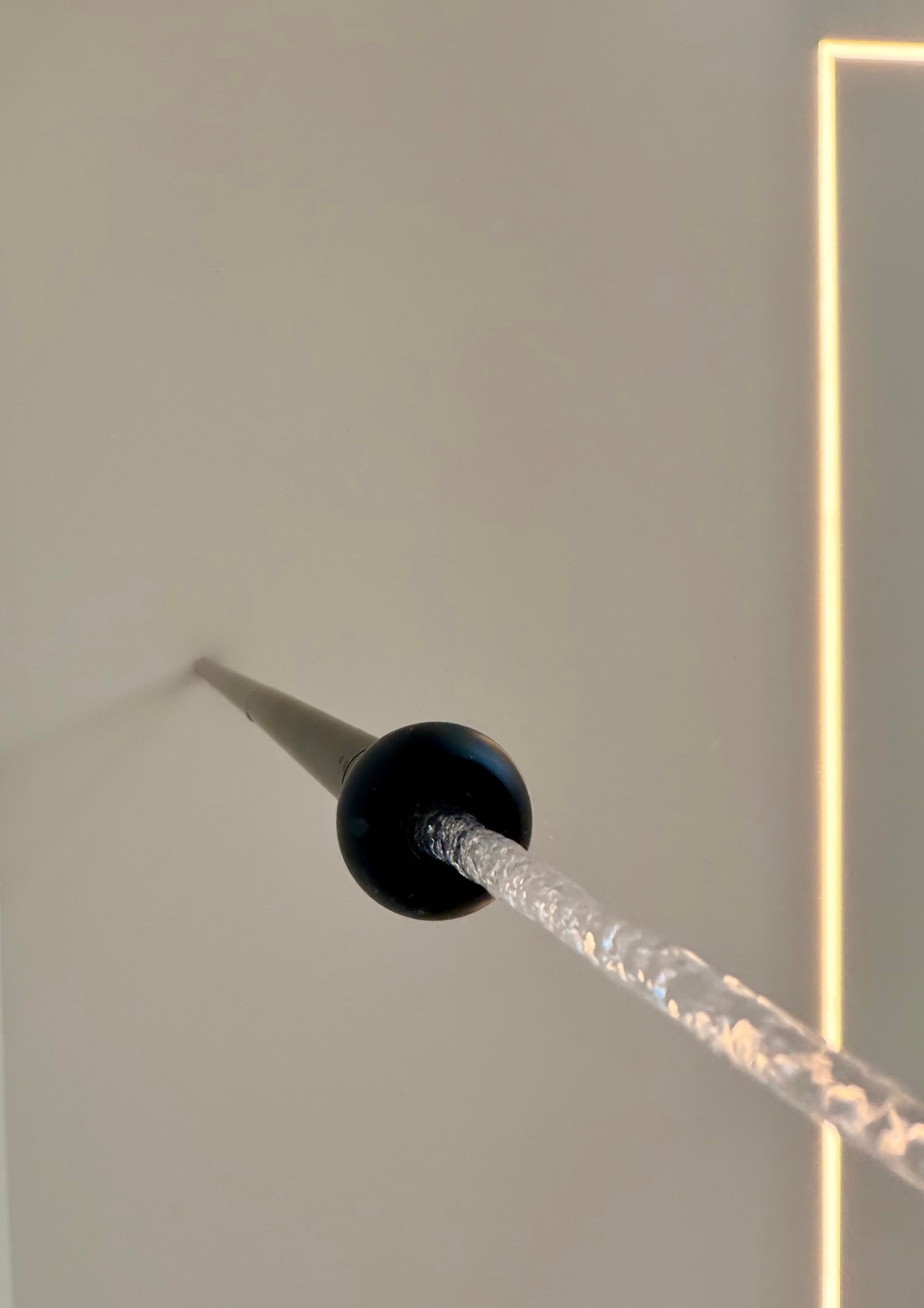 Black nail with textured silver head against beige wall with gold neon line