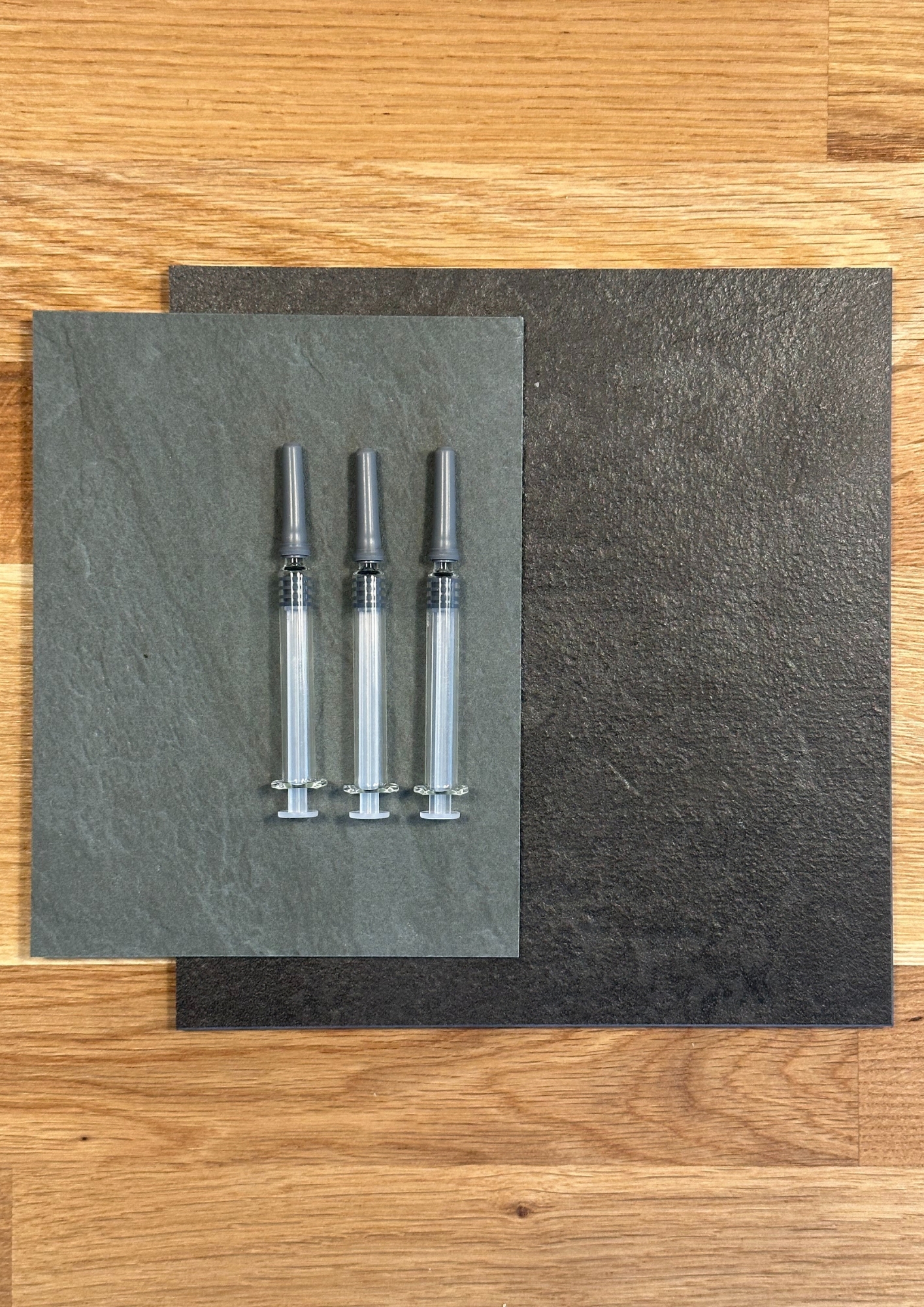 Three medical syringes arranged on slate tiles, displayed on wooden floor