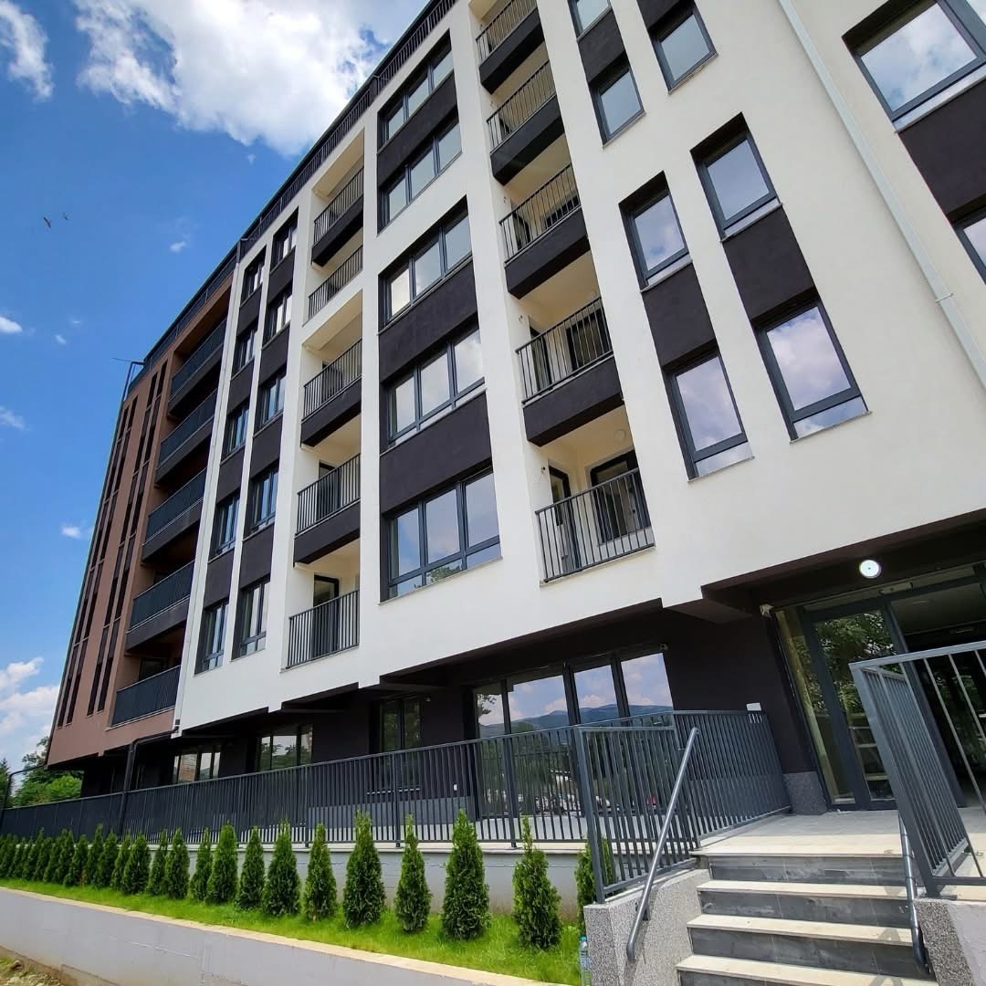 Modern multi-story apartment building with white and brown facade, balconies, and landscaping.