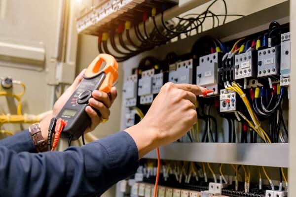 An electrician holds a digital multimeter to check the voltage of a commercial building's wiring