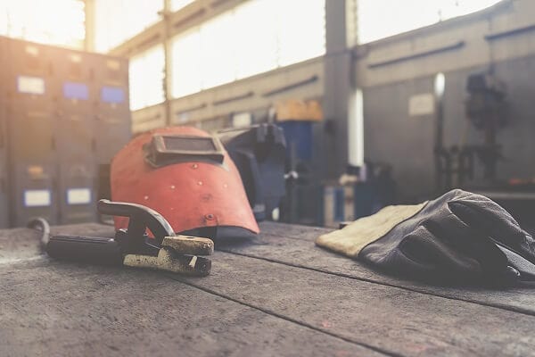 A welder's mask and gloves lay on a bench