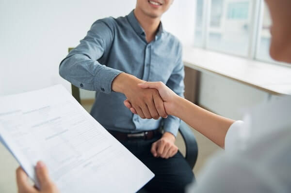A person in a button-down shirt shakes the interviewer's hand