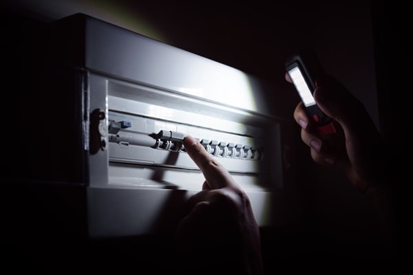 An electrician uses a flashlight to inspect an electrical box during a blackout