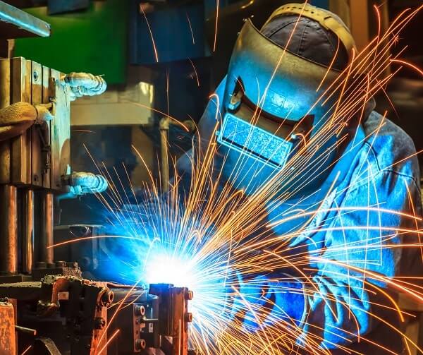 A welder in safety gear manually welds a project in the shop