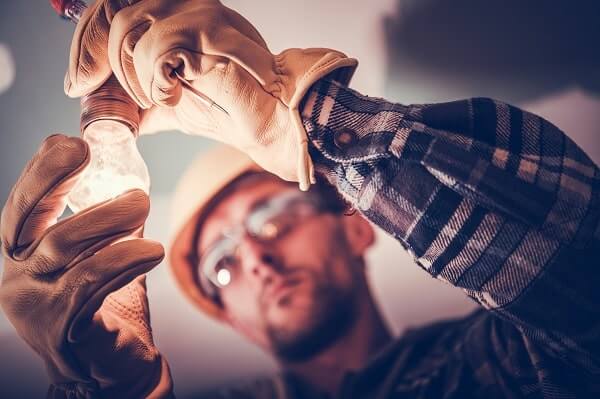 An electrician handles a lightbulb while wearing work gloves