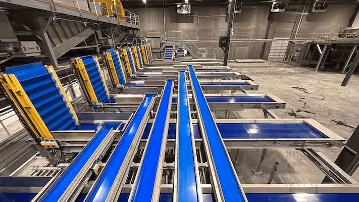 Empty industrial conveyor belts with blue surfaces and yellow supports inside a large warehouse.