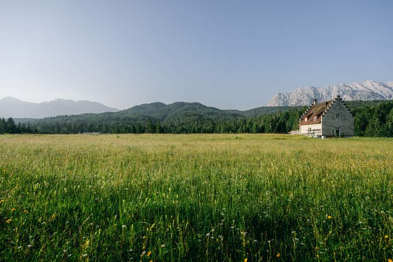 Building in the middle of a vaste green meadows with Alps in the back.