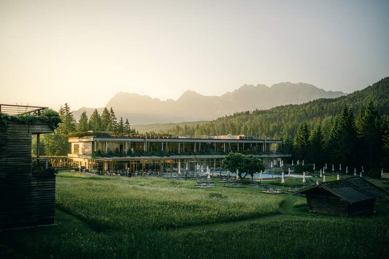 A hotel in the a green field with Alps in the background.