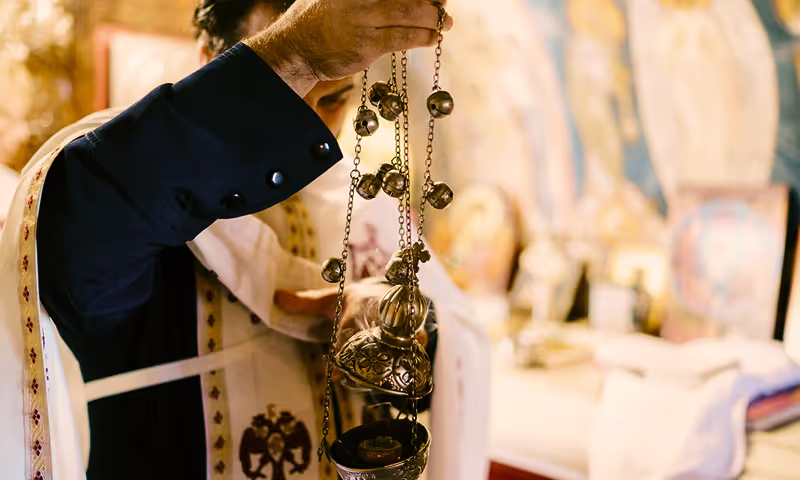 Orthodox priest preparing the censer with incense during the Divine Liturgy, symbolizing prayers rising to heaven and the sanctification of the faithful.