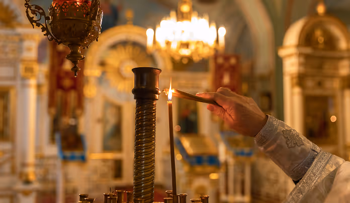 Faithful priest lights candle in majestic Christian church with ornate, elegant decorations.