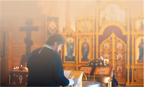 A devoted Orthodox Christian in prayer before sacred-icons and holy scripture in a church.