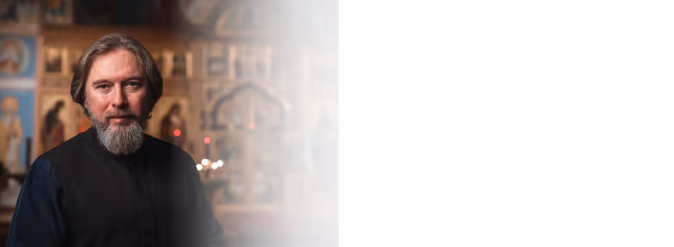 Orthodox priest in white vestments reading the Gospel beside a chalice.