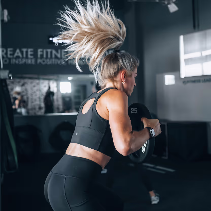 A woman with blonde hair and a black tank top lifting a weight.