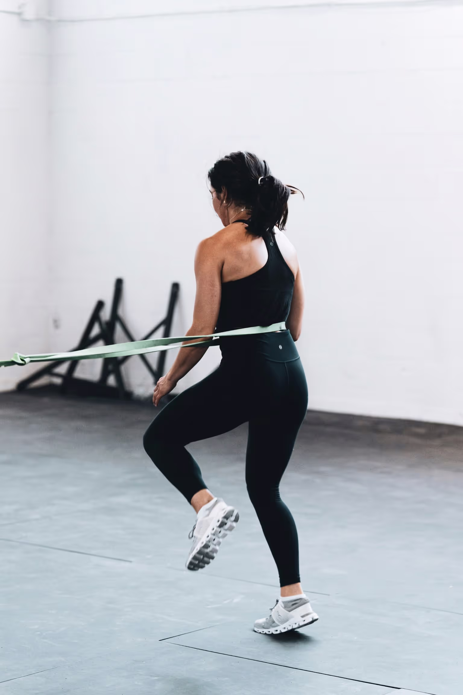 A woman wearing black pants and a black shirt is jumping on a trampoline.