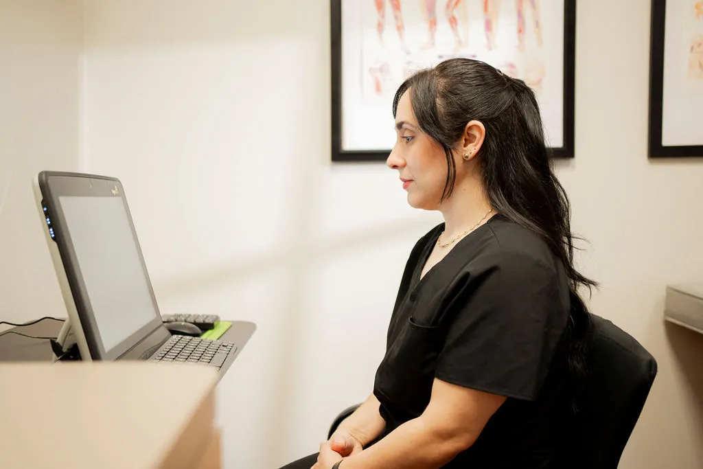 Medical professional preparing to work on Functional Vision and Oculomotor Assessment, seated at a computer in a modern clinic office.