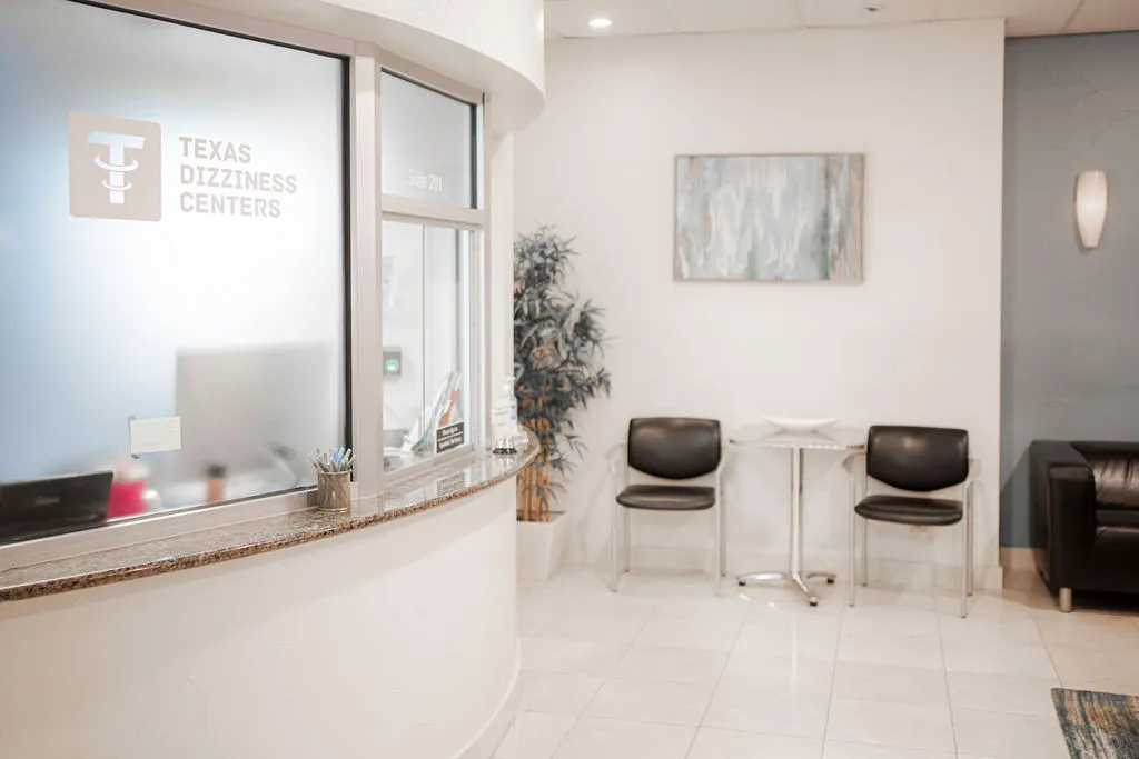Front desk and waiting area of Texas Dizziness Centers, showing the clinic logo on frosted glass, with comfortable seating and a welcoming atmosphere.