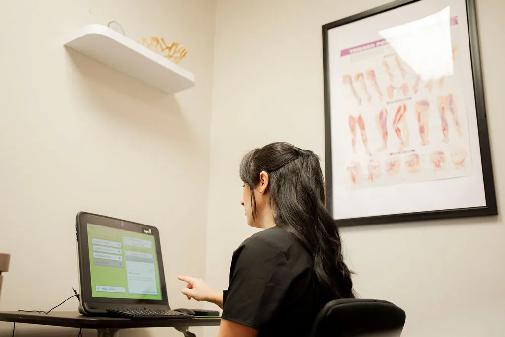 Medical professional preparing to work on Functional Vision and Oculomotor Assessment, seated at a computer in a modern clinic office.