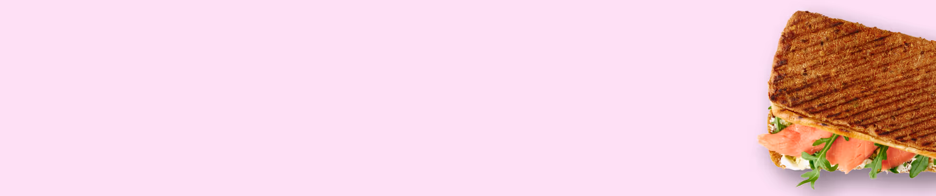 Gegrilltes Vollkorn-Sandwich mit Lachs und Rucola auf rosa Hintergrund.