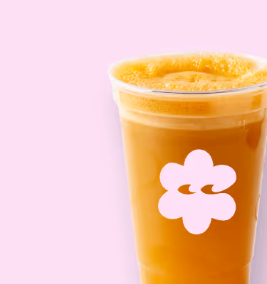 Becher mit frisch gepresstem Orangensaft vor hellrosa Hintergrund.