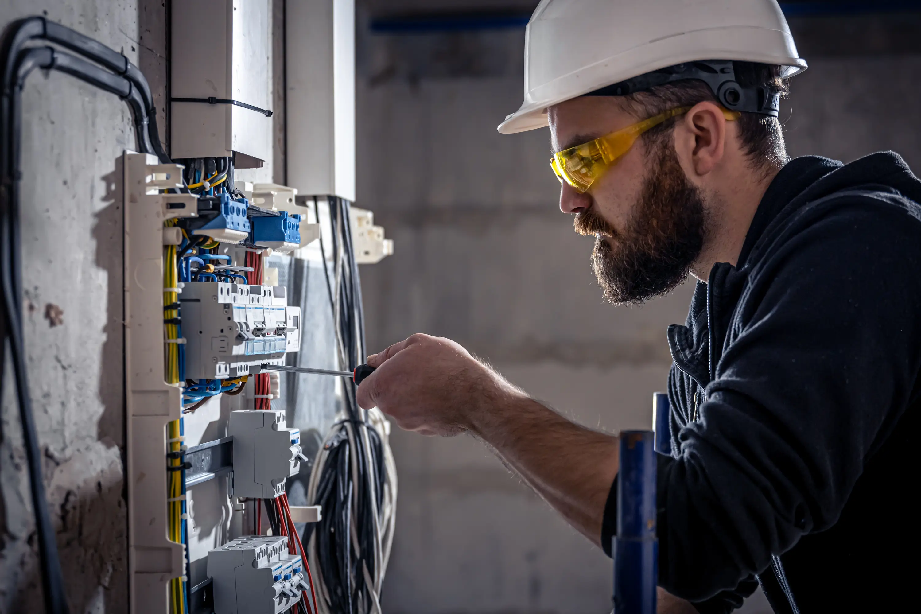 Électricien concentré en train de visser un composant dans un tableau électrique
