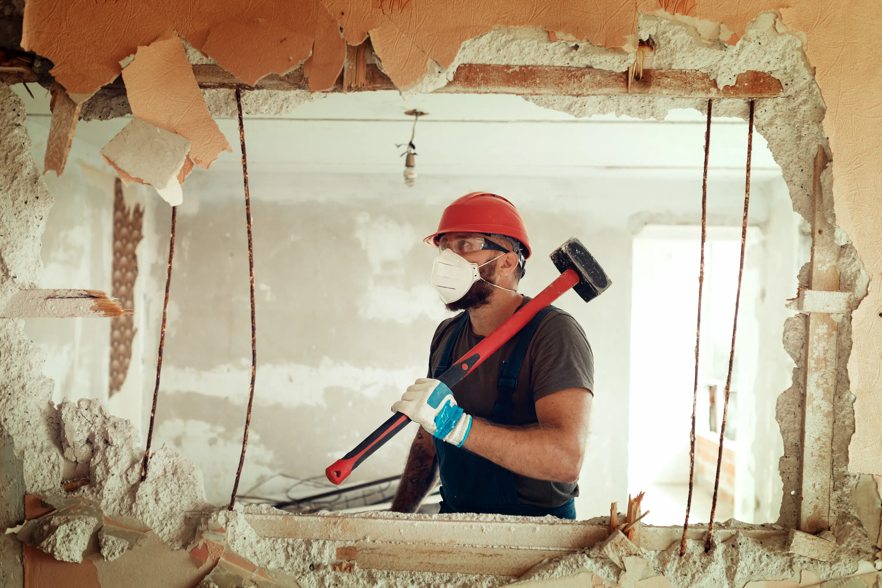 Ouvrier en pleine démolition d’un mur, équipé d’un casque et d’une masse