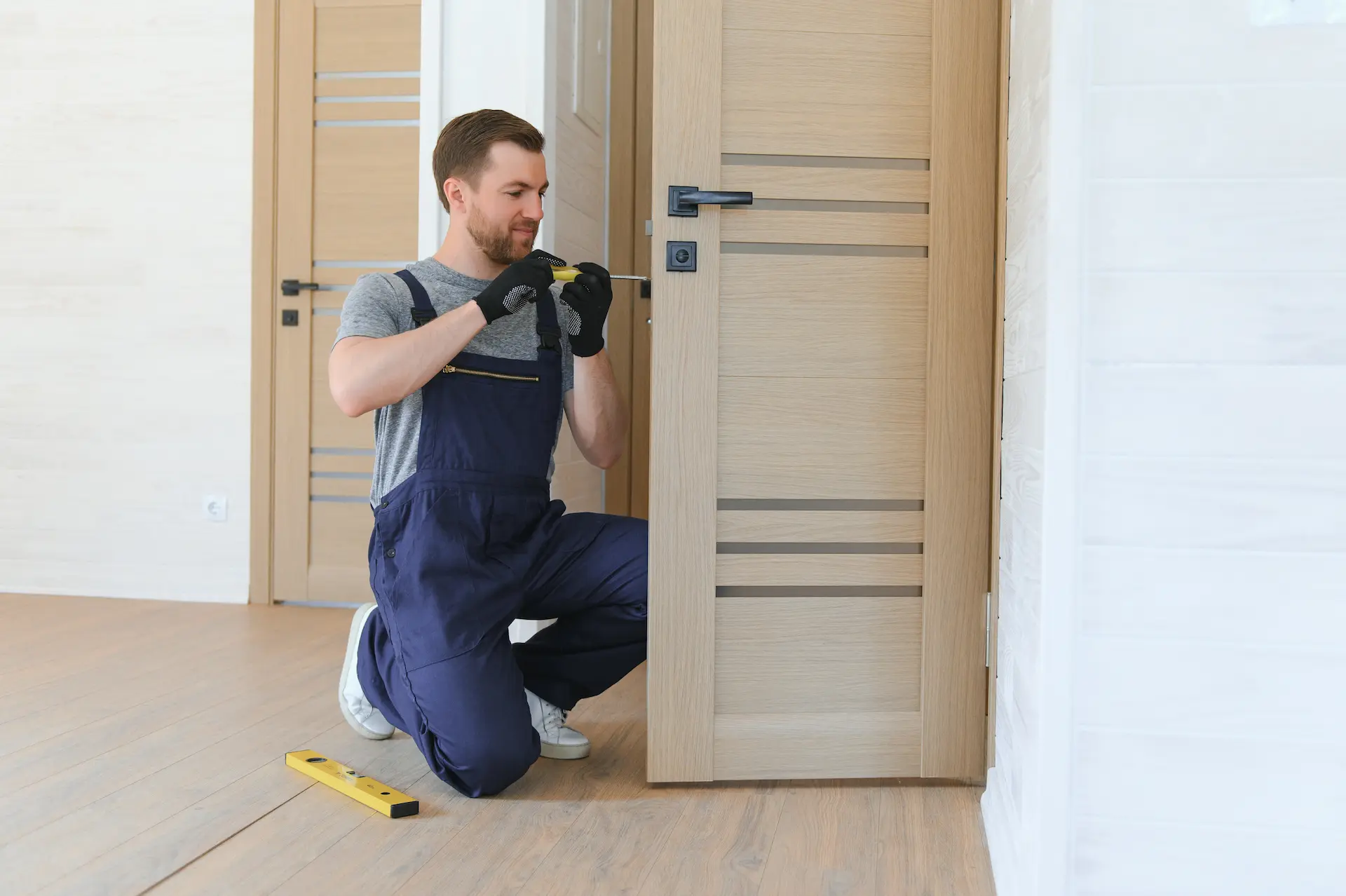 Serrurier installant une serrure sur une porte en bois dans un intérieur lumineux