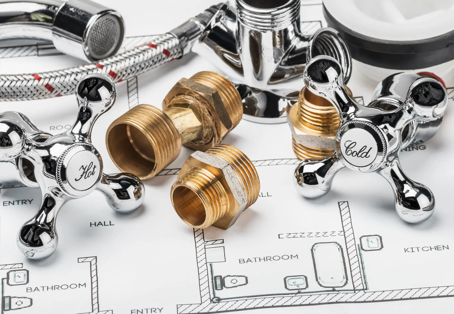 Pièces de plomberie en laiton et poignées de robinet posées sur un plan de maison technique