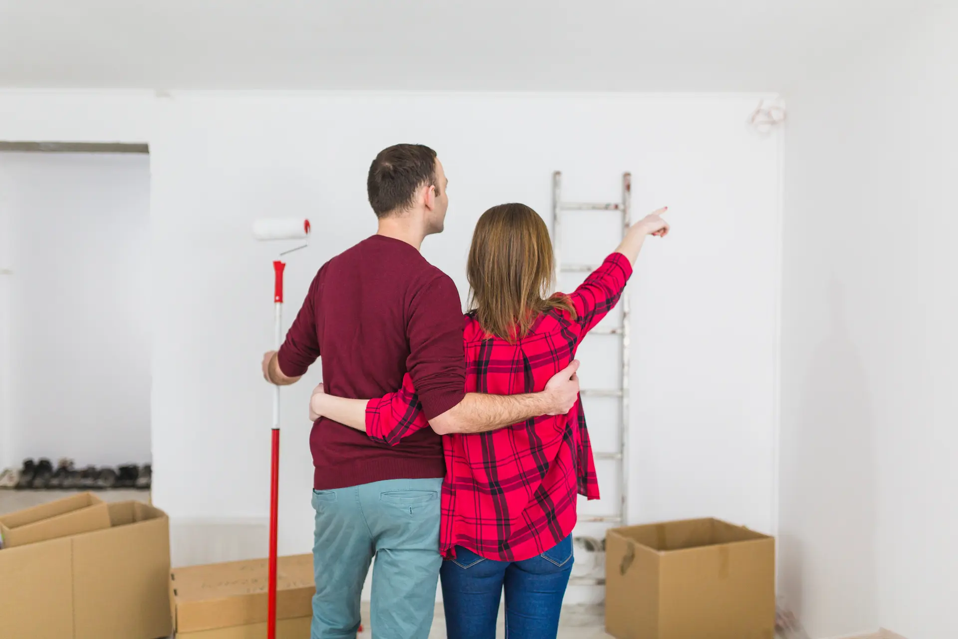 Couple de particuliers préparant la rénovation d’une pièce avec rouleau de peinture et cartons