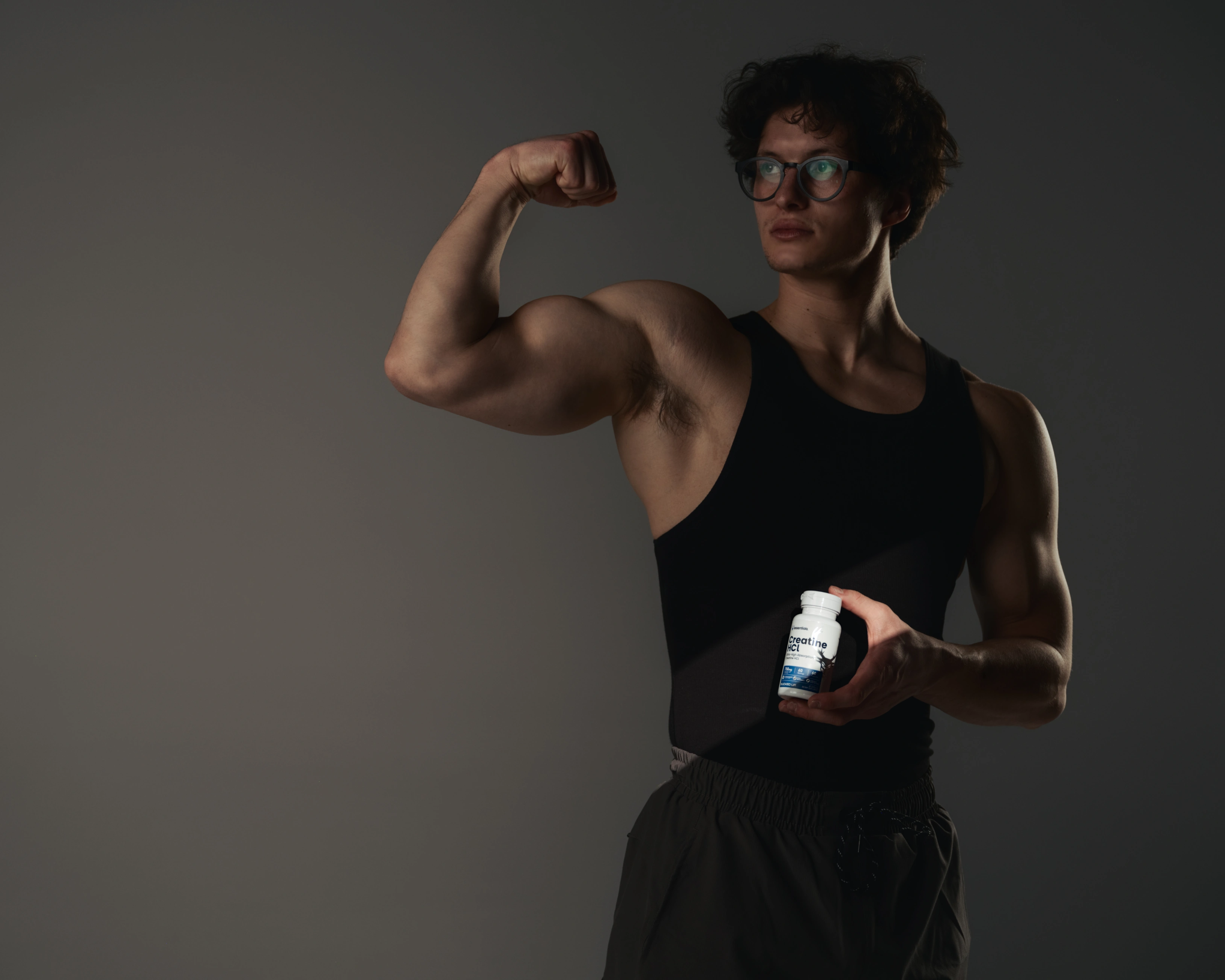 Man flexing in a shadow holding Bucked Up Creatine HCl, a new Creatine product.