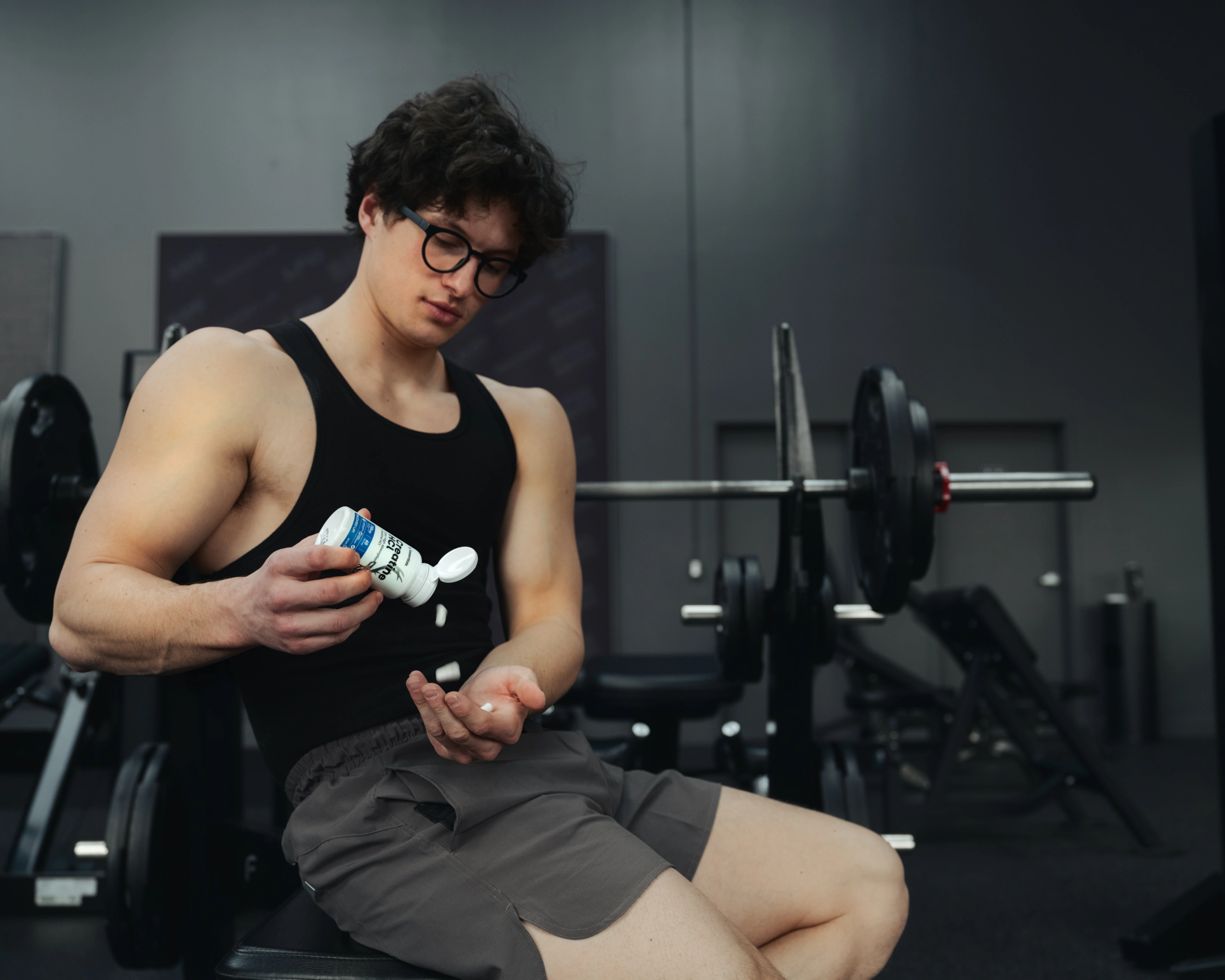 Man pouring out a couple of Bucked Up Creatine HCl capsules in the gym next to a bench press.