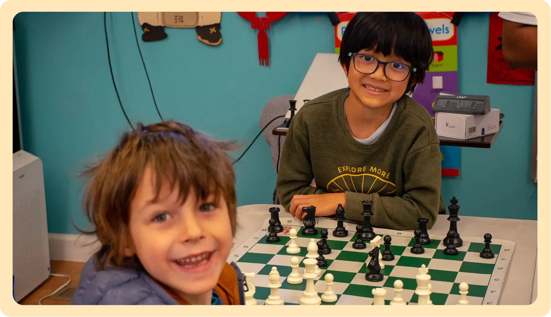 Two young boys smile while sitting at a chess board during a lesson, highlighting the fun and social environment of the academy.