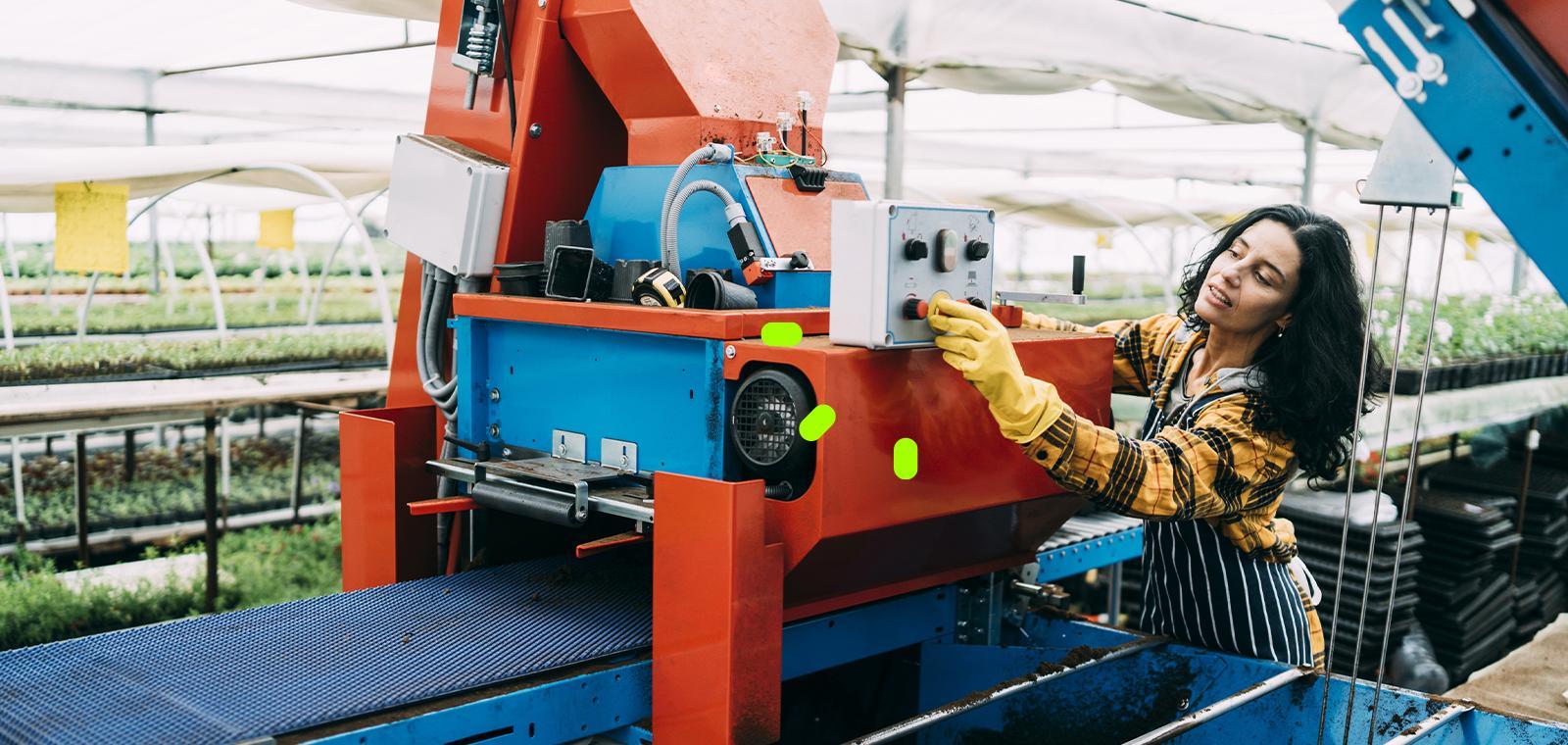 3A woman is engaged in machine work within a greenhouse, with lush plants growing in the background