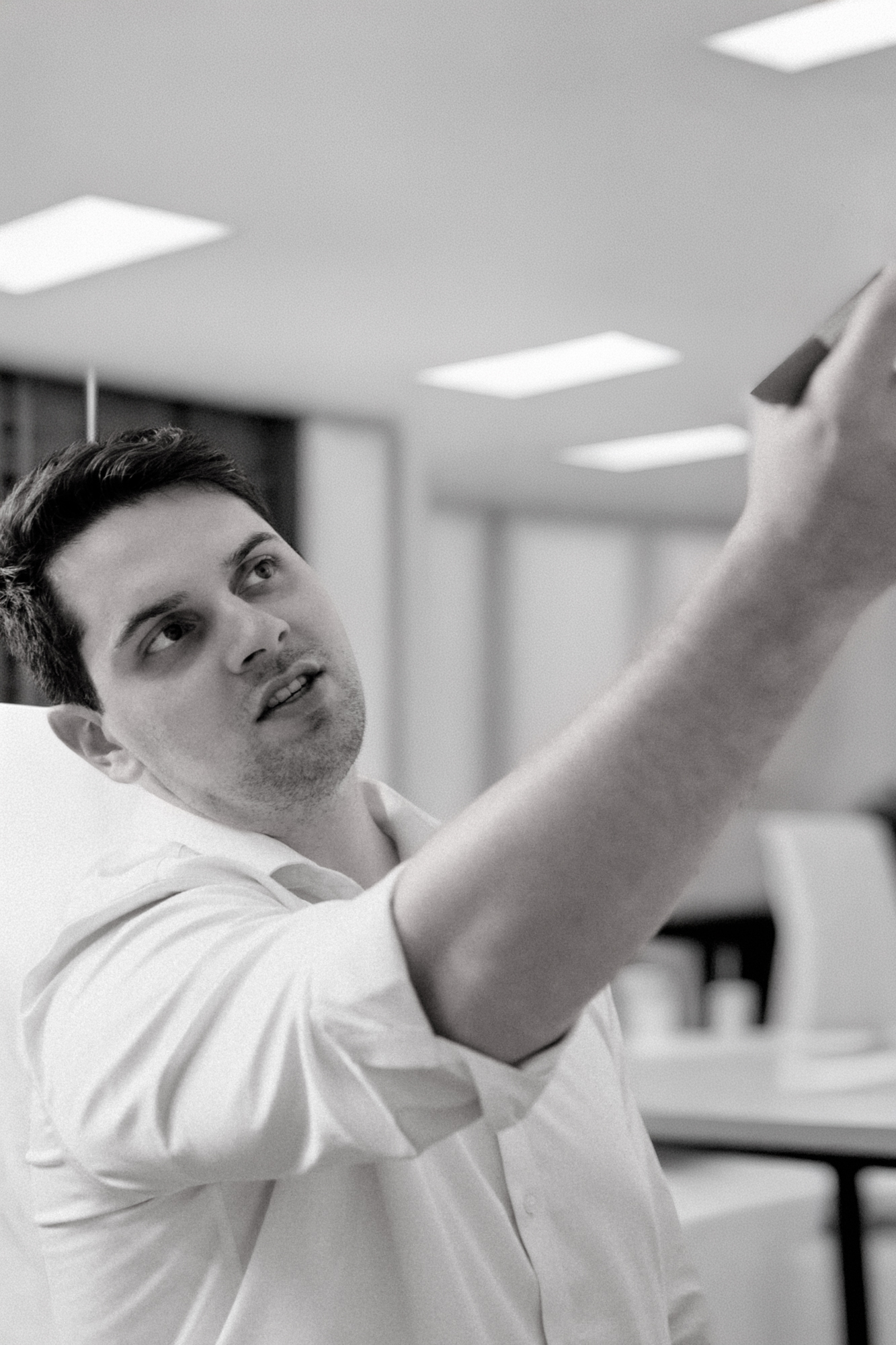 Young man in white shirt reaching upward with focus in a modern office setting.