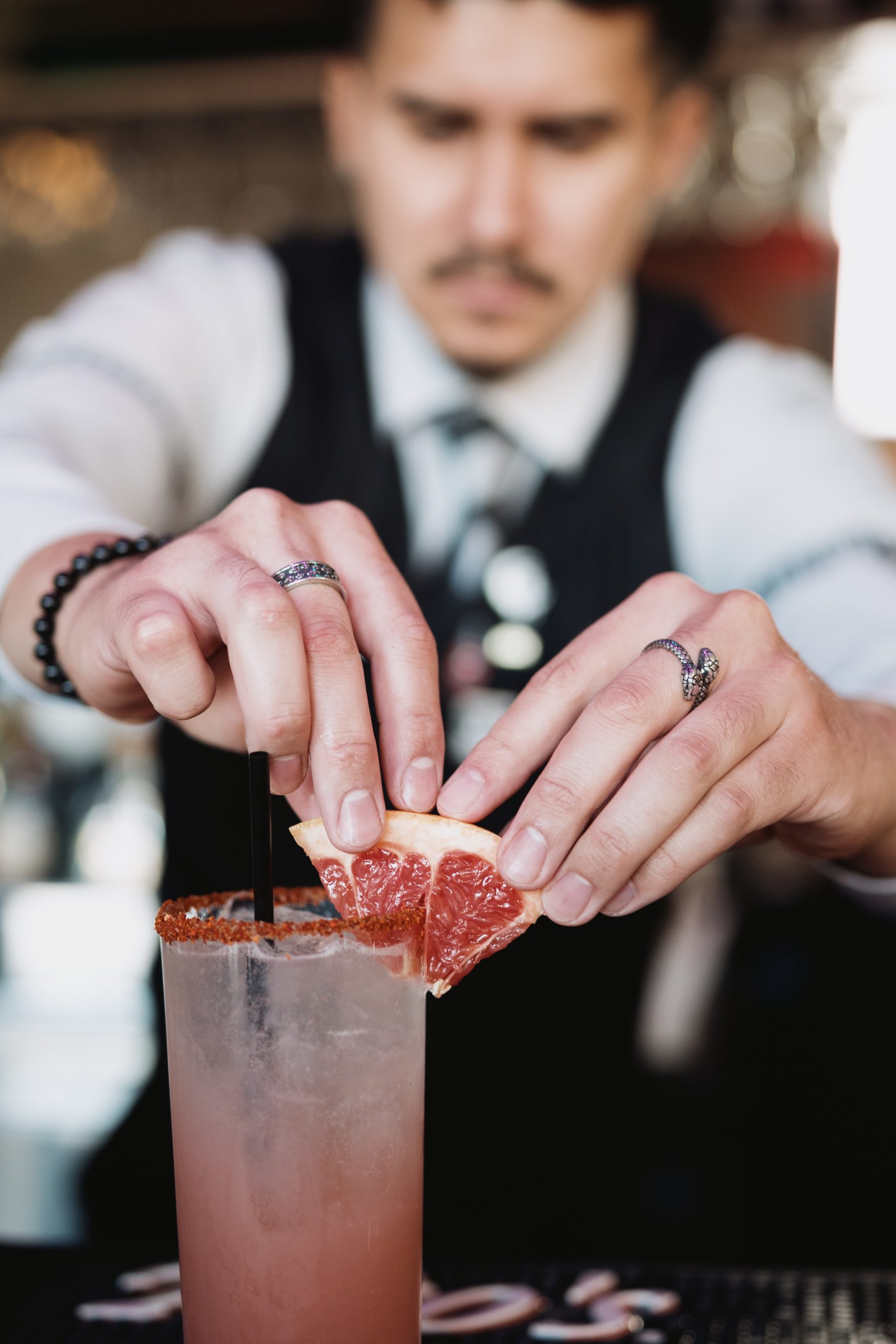 Bartender garnishing a pink cocktail with a grapefruit slice at a bar.