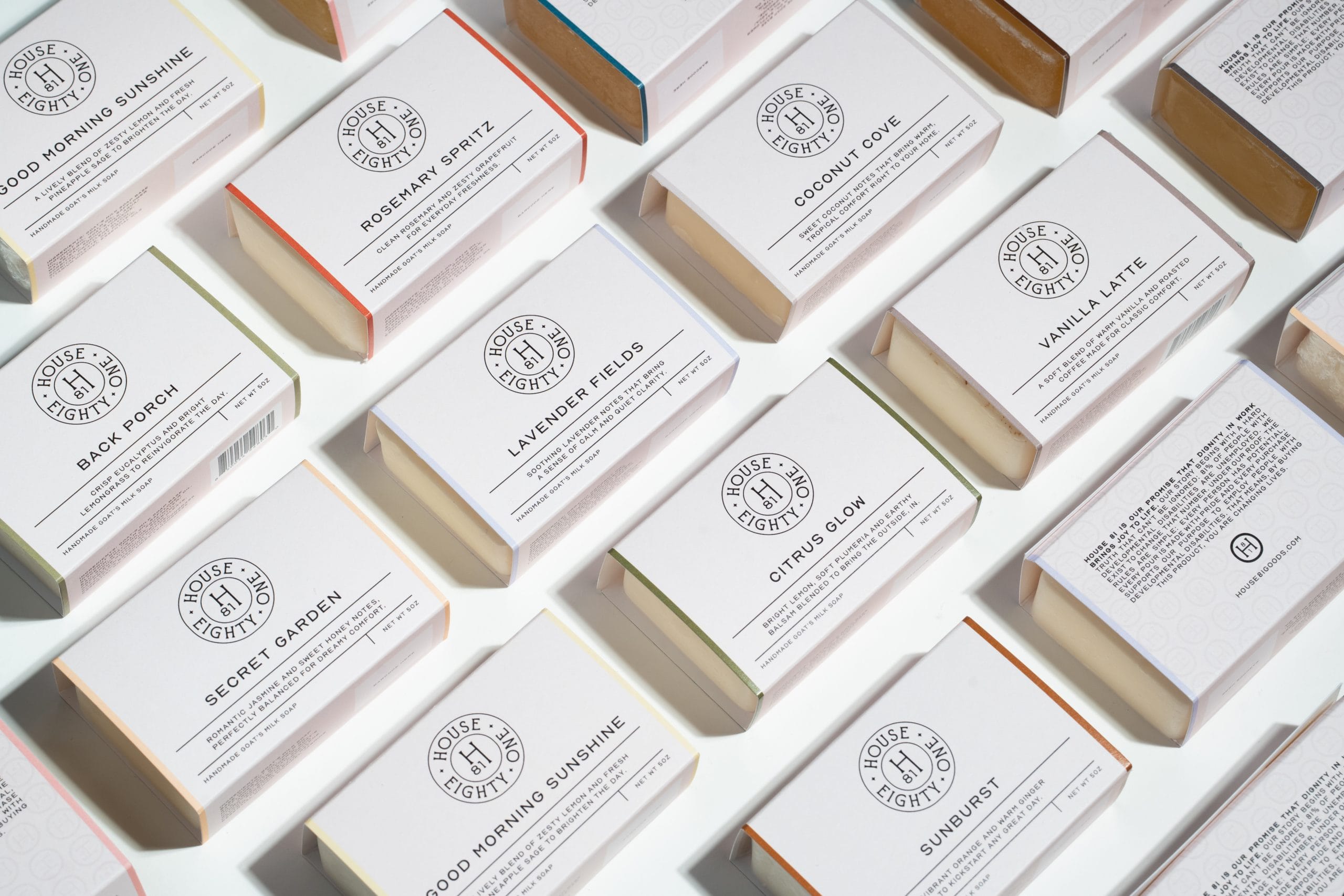 Assorted House Eighty One branded handmade goat's milk soap bars in white boxes with colored accents.