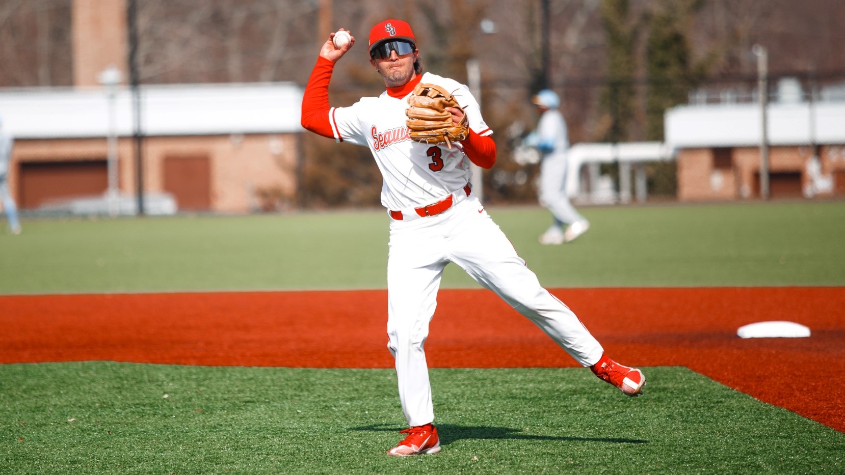 Baseball player in white and red uniform throwing a ball on a field near first base.