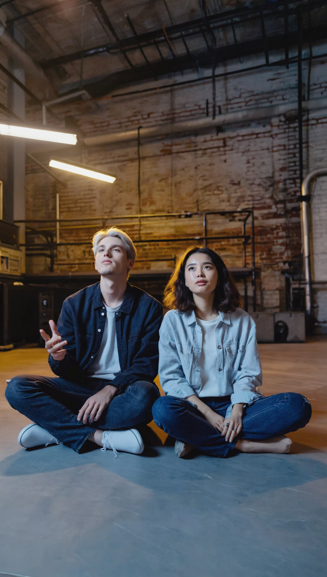 two people sitting on concrete floor crosslegged in jeans