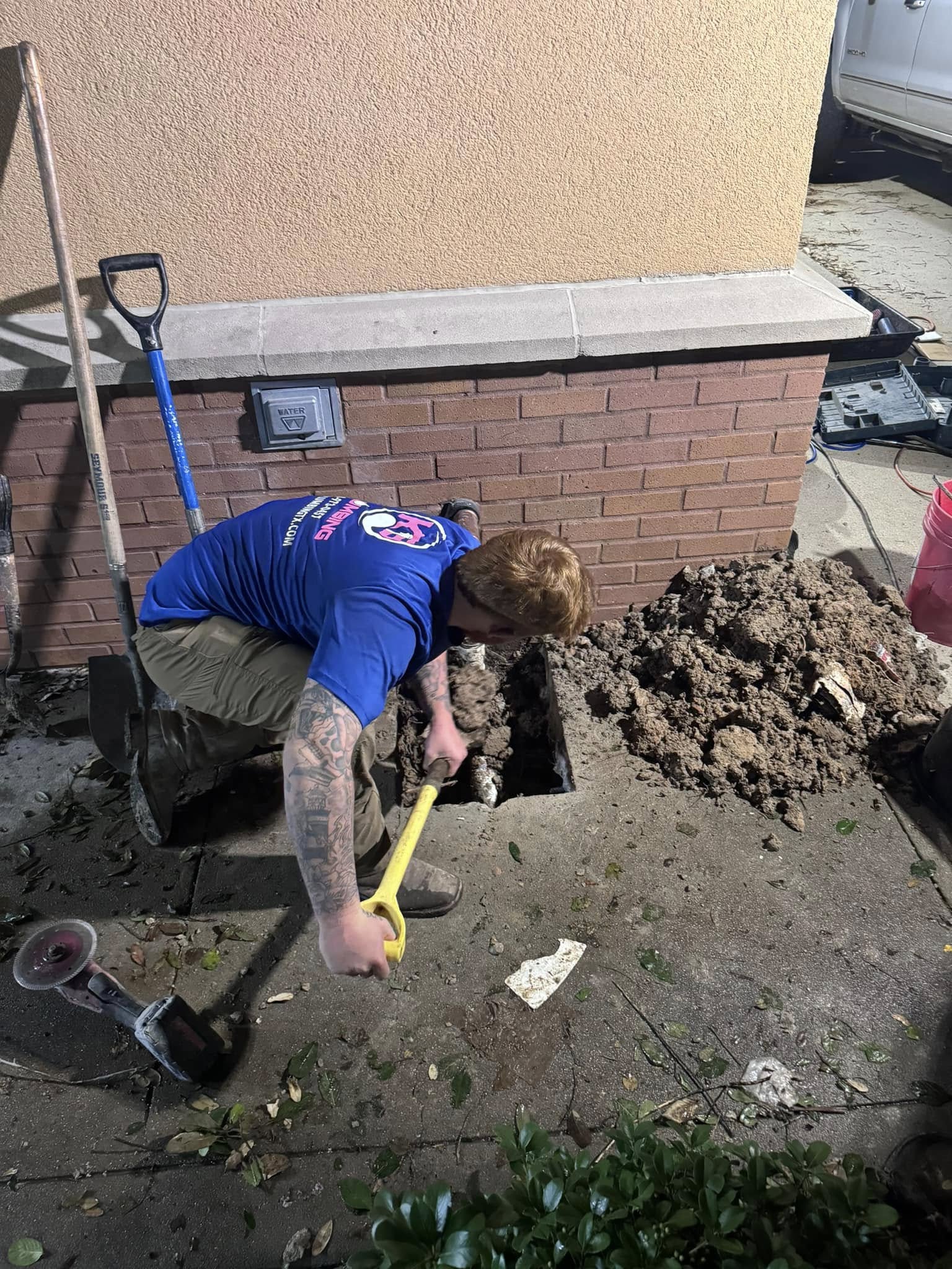Plumber digging beside a brick wall to repair an underground pipe.