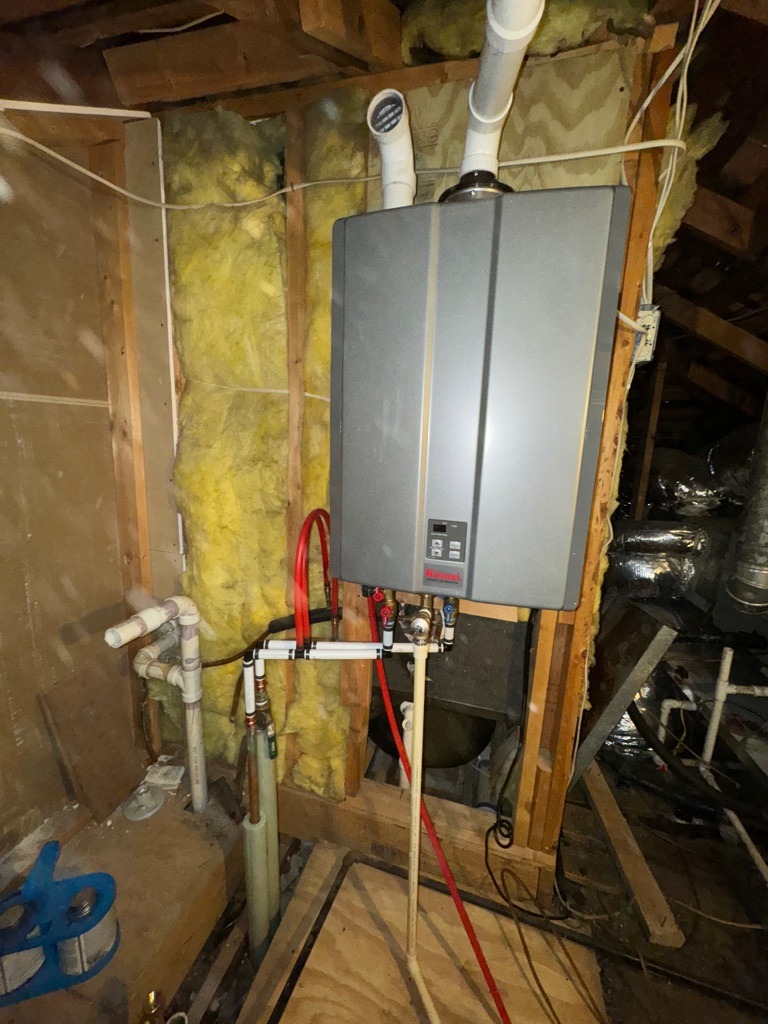 Tankless water heater installed in an attic with visible piping.