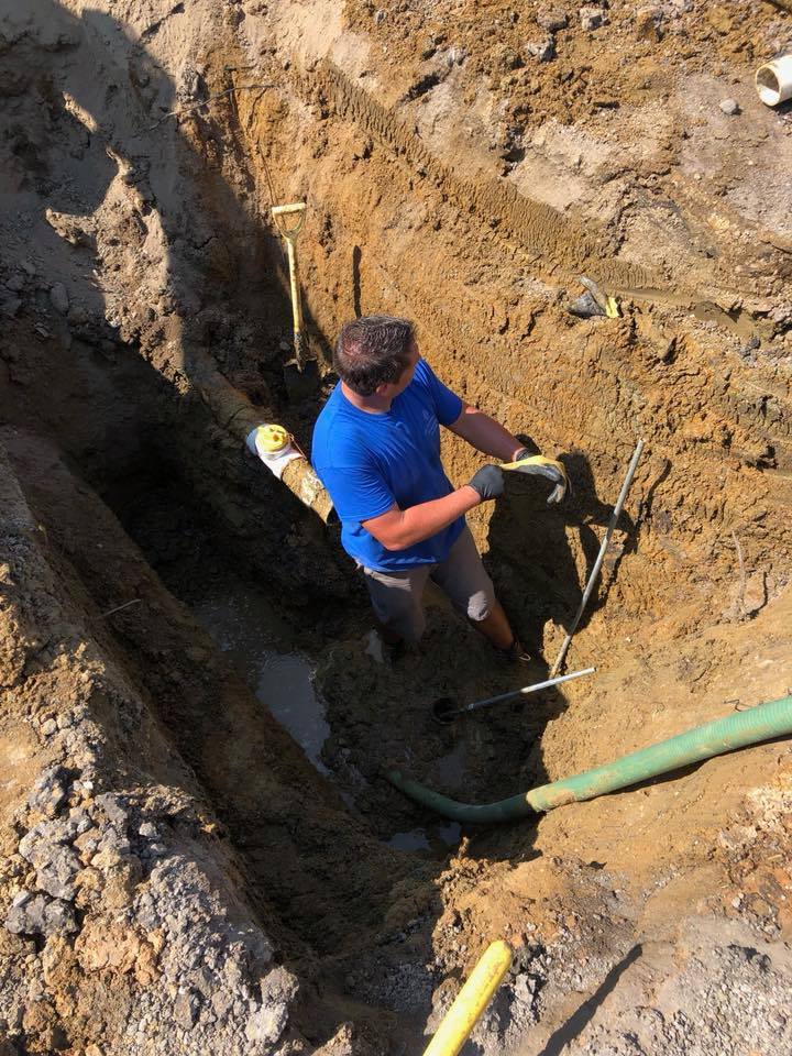 A plumber working in a trench, handling pipes for a sewer repair.