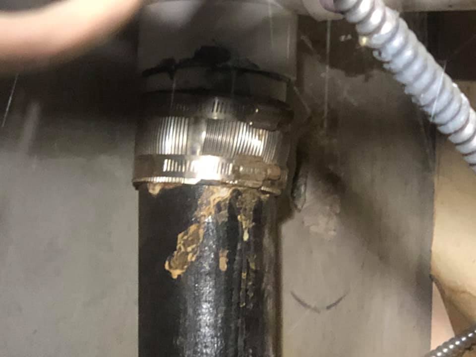Leaking pipe connection with metal clamps under a sink.