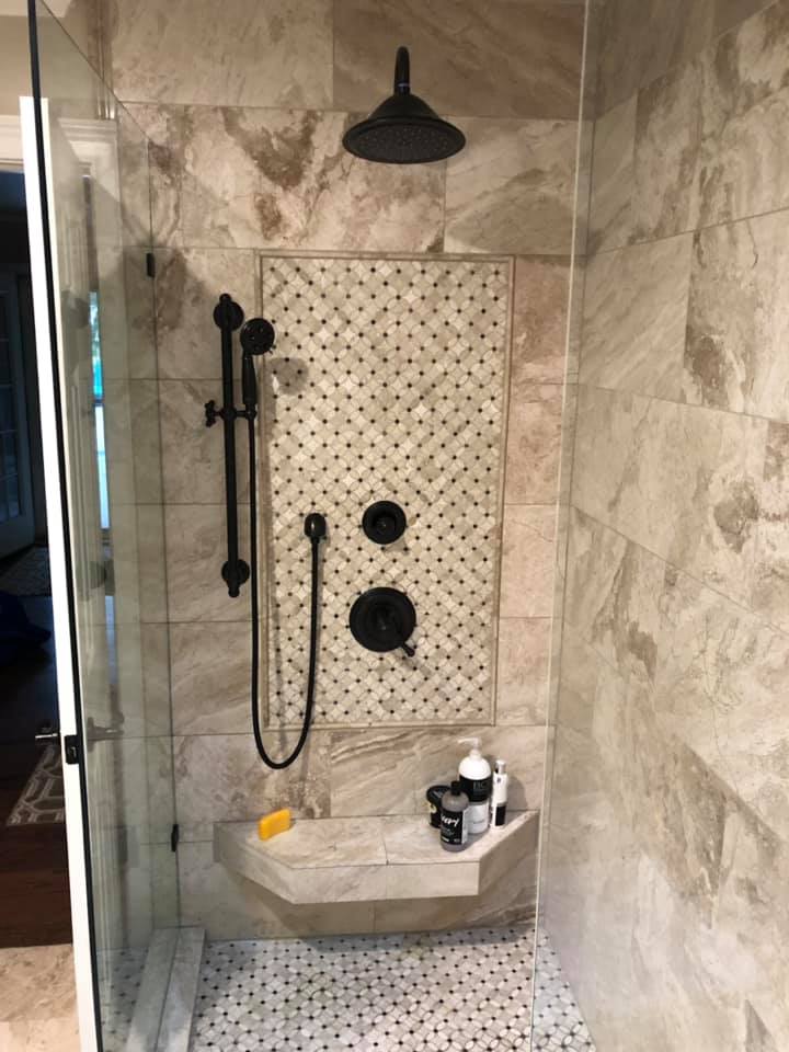 Modern shower with a black rainfall showerhead, handheld shower, and tiled wall with toiletries on a built-in shelf.
