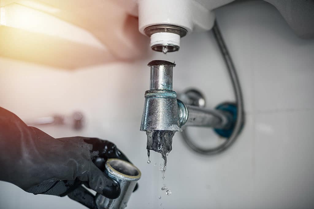 Close-up of a leaking faucet being repaired with a hand holding a metal part.