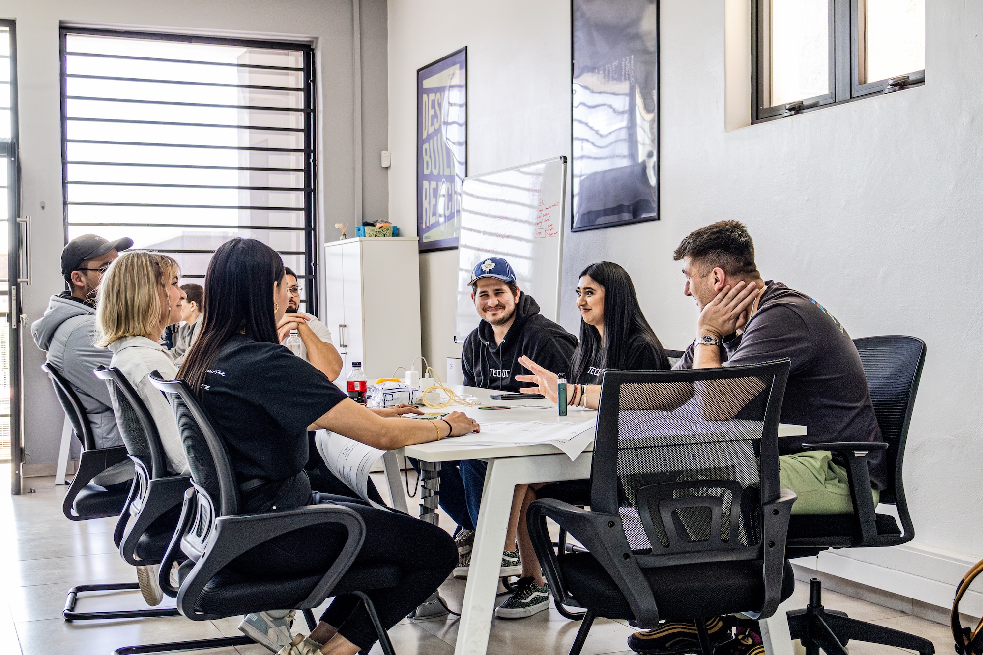 Man in black hoodie working on a laptop displaying a graphic design software at a desk in an office at Tecbot.