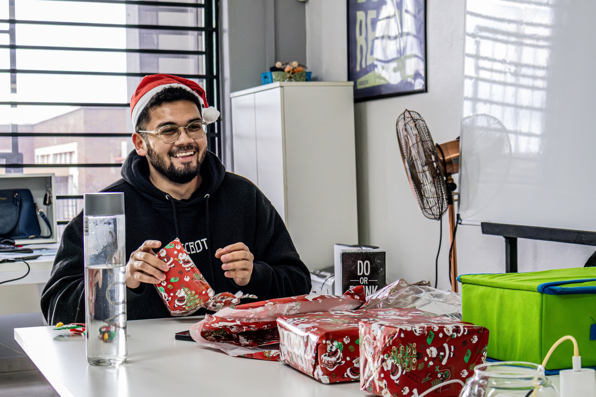 Man in black hoodie working on a laptop displaying a graphic design software at a desk in an office at Tecbot.
