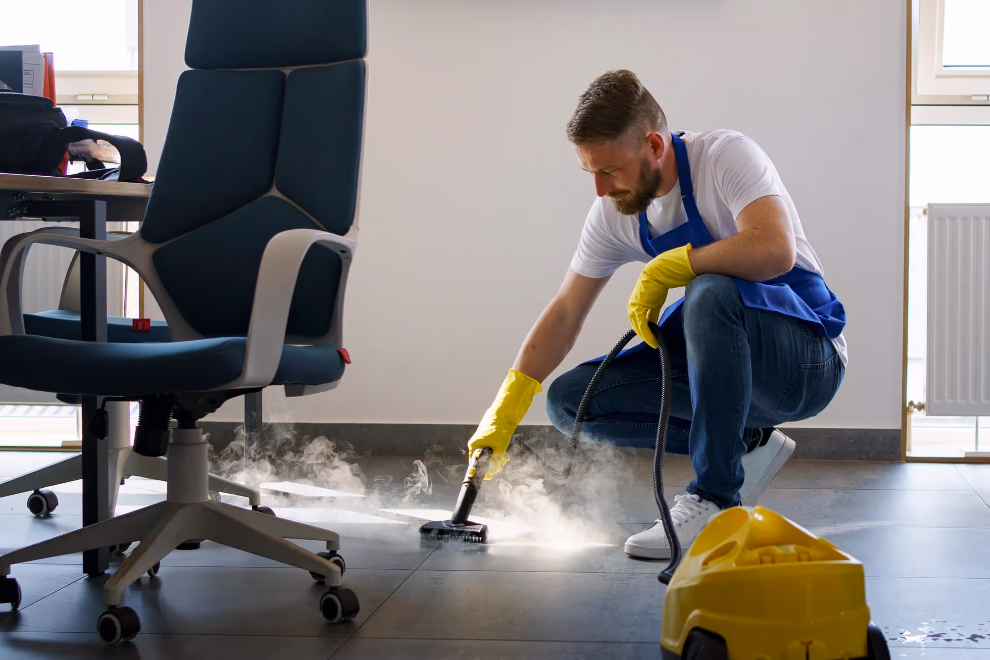 A man kneeling down while steam cleaning grout and tiles