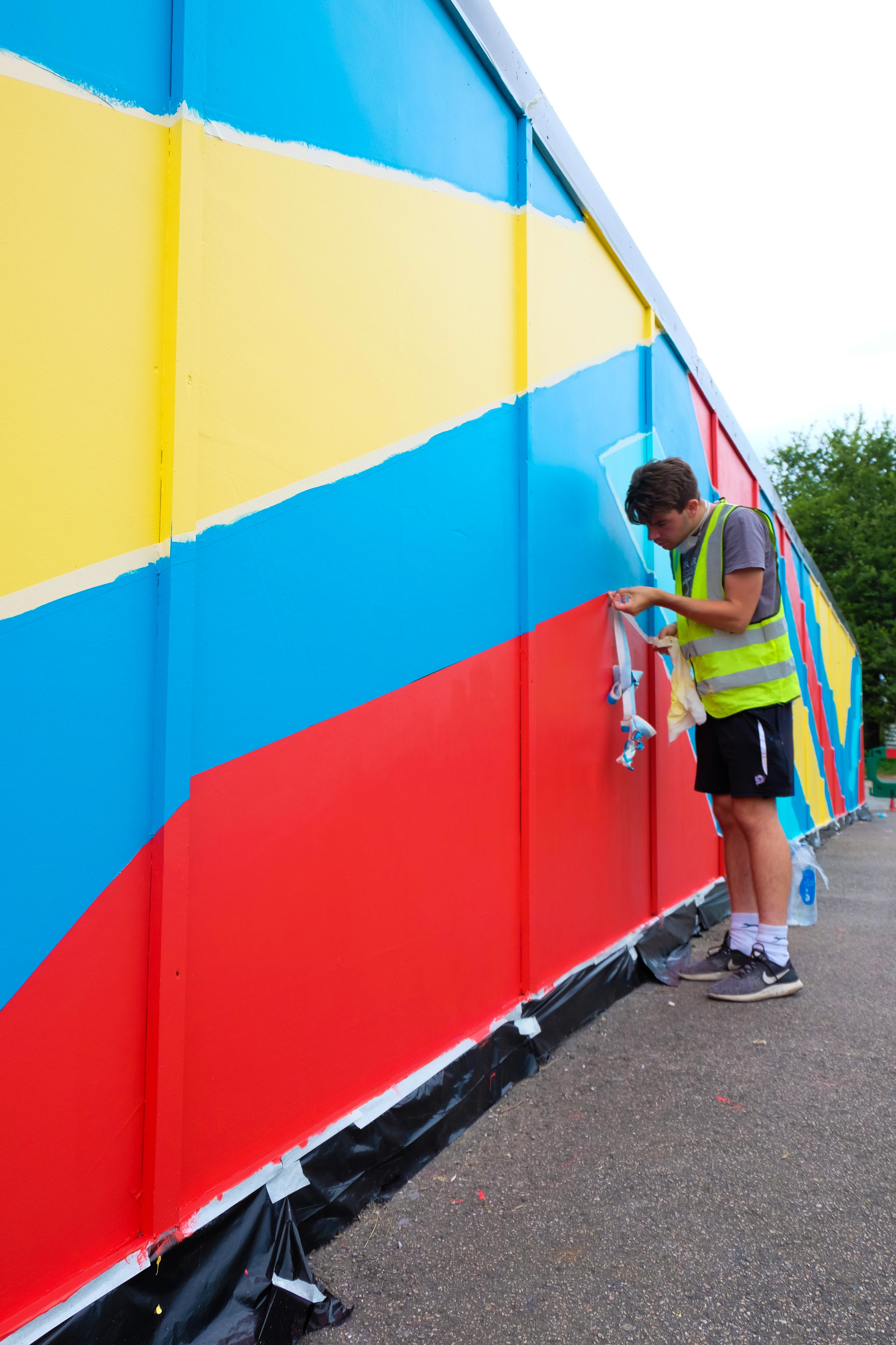Artists hand-painting the outdoor mural installation in Sittingbourne on hoarding boards